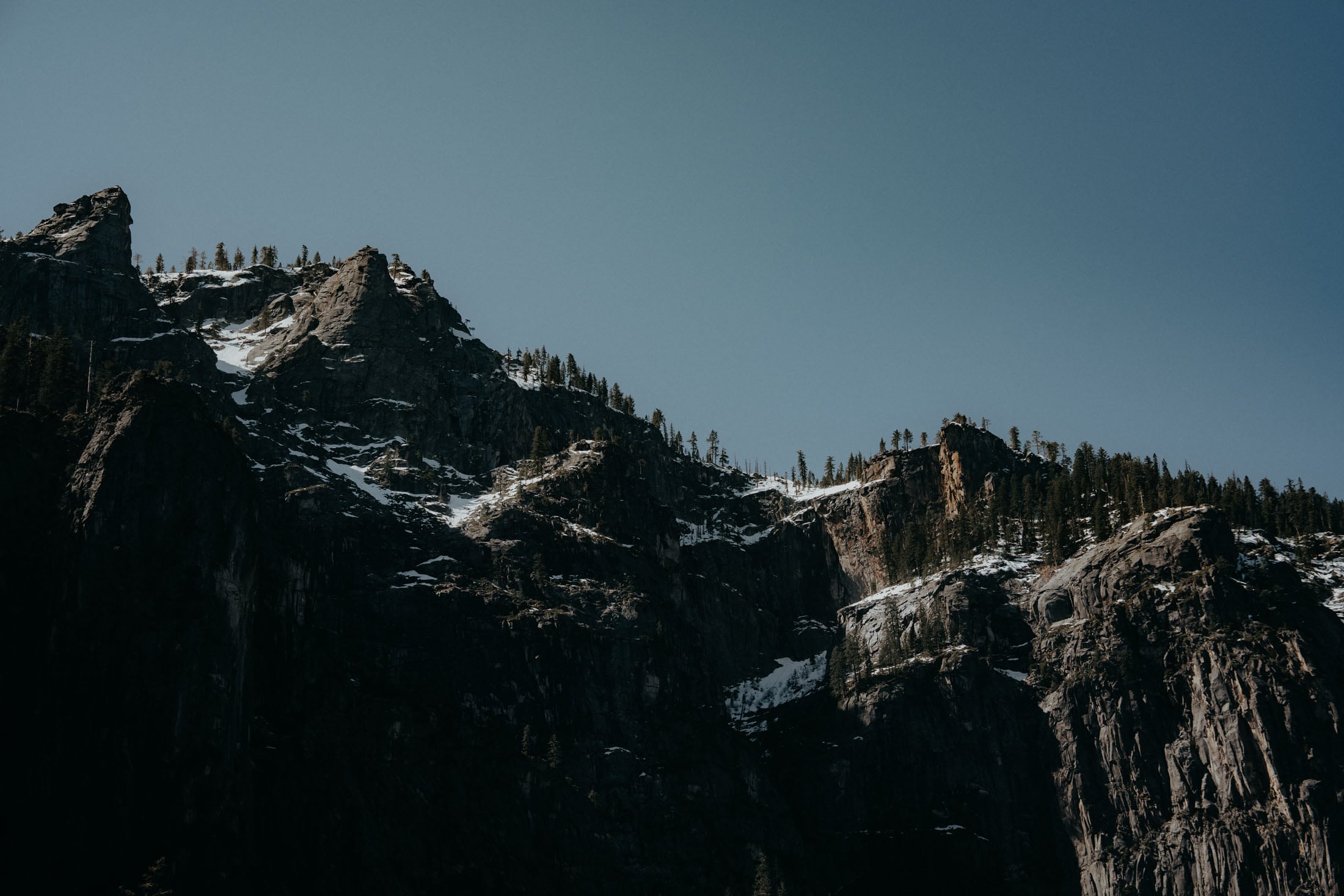 Majestic rocky mountains under a clear blue sky, with sparse vegetation on the peaks.