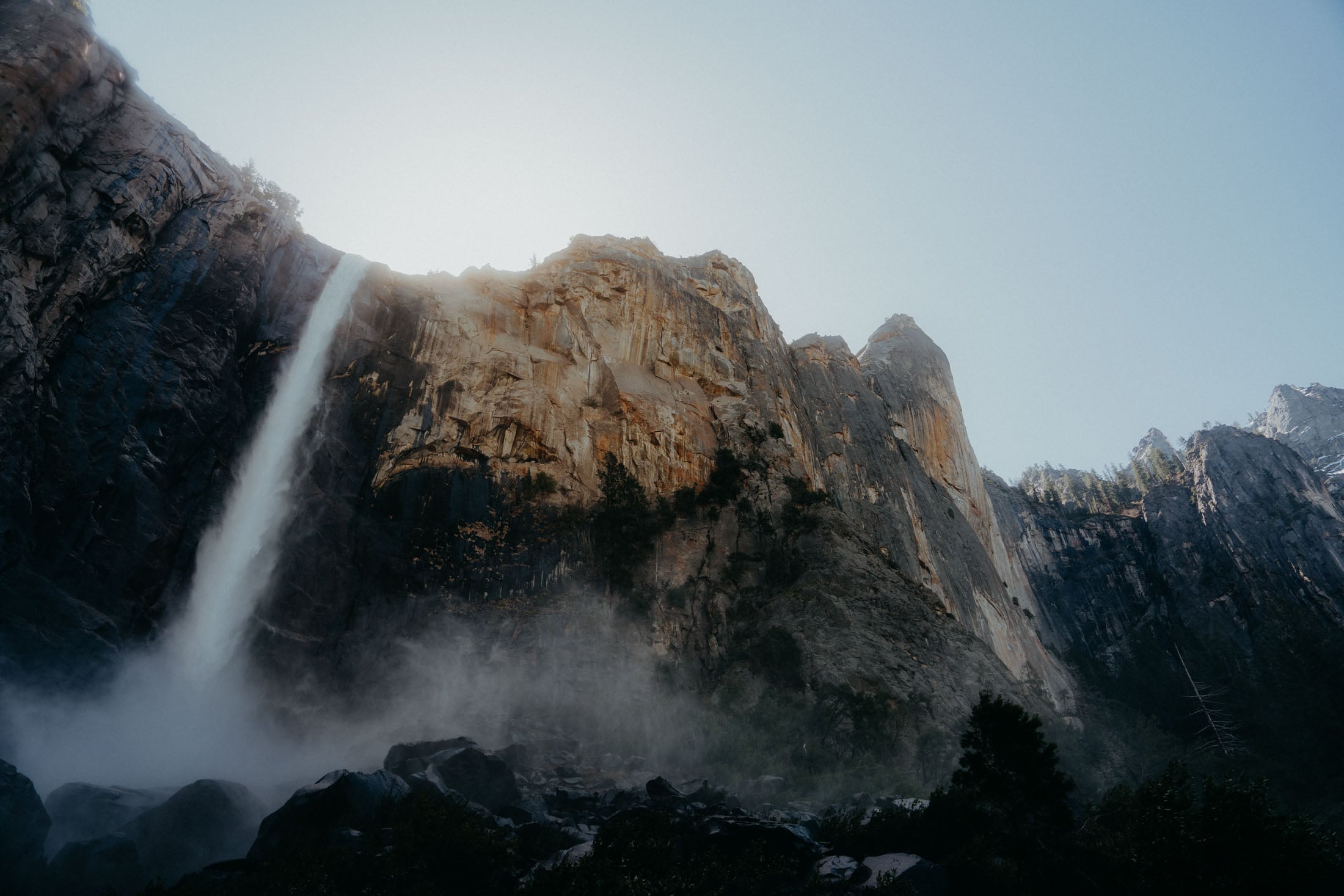A stunning view of a waterfall cascading down a rocky cliff in Yosemite National Park, with sunlight illuminating the scene.
