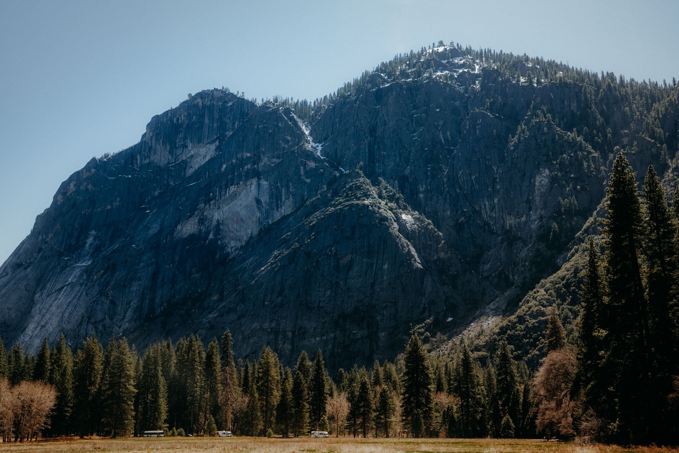 A breathtaking view of towering cliffs and lush green trees in Yosemite National Park, with a clear blue sky above.