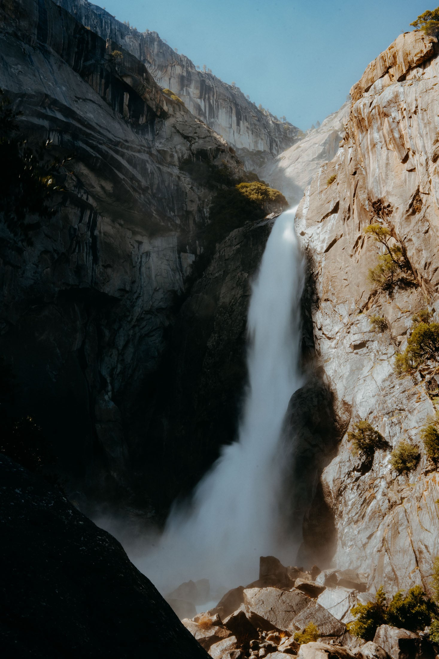 A breathtaking waterfall cascading down rocky cliffs in Yosemite National Park, surrounded by lush trees and sunlight filtering through the mist.
