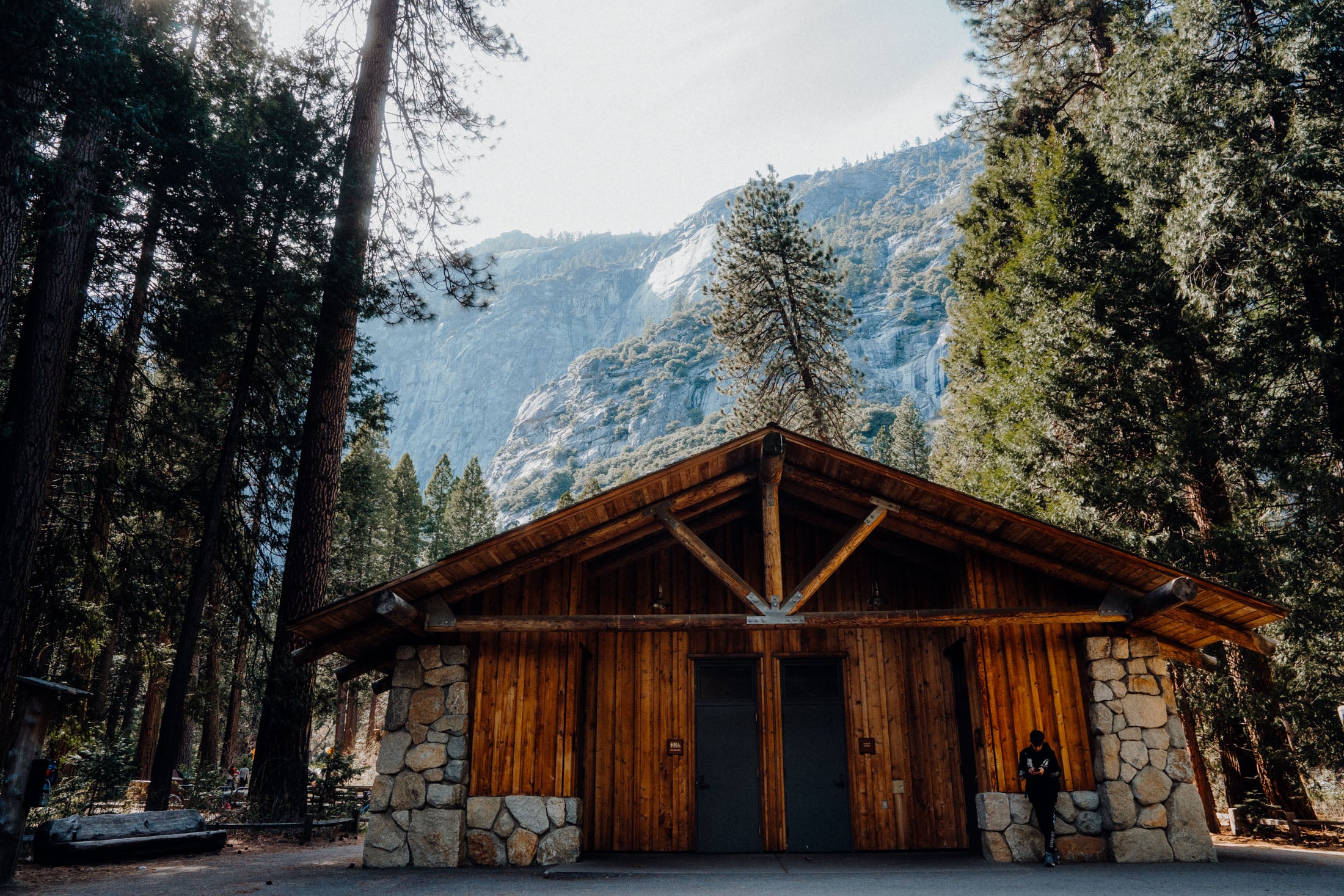 A rustic wooden building surrounded by tall trees and rocky cliffs in Yosemite National Park.