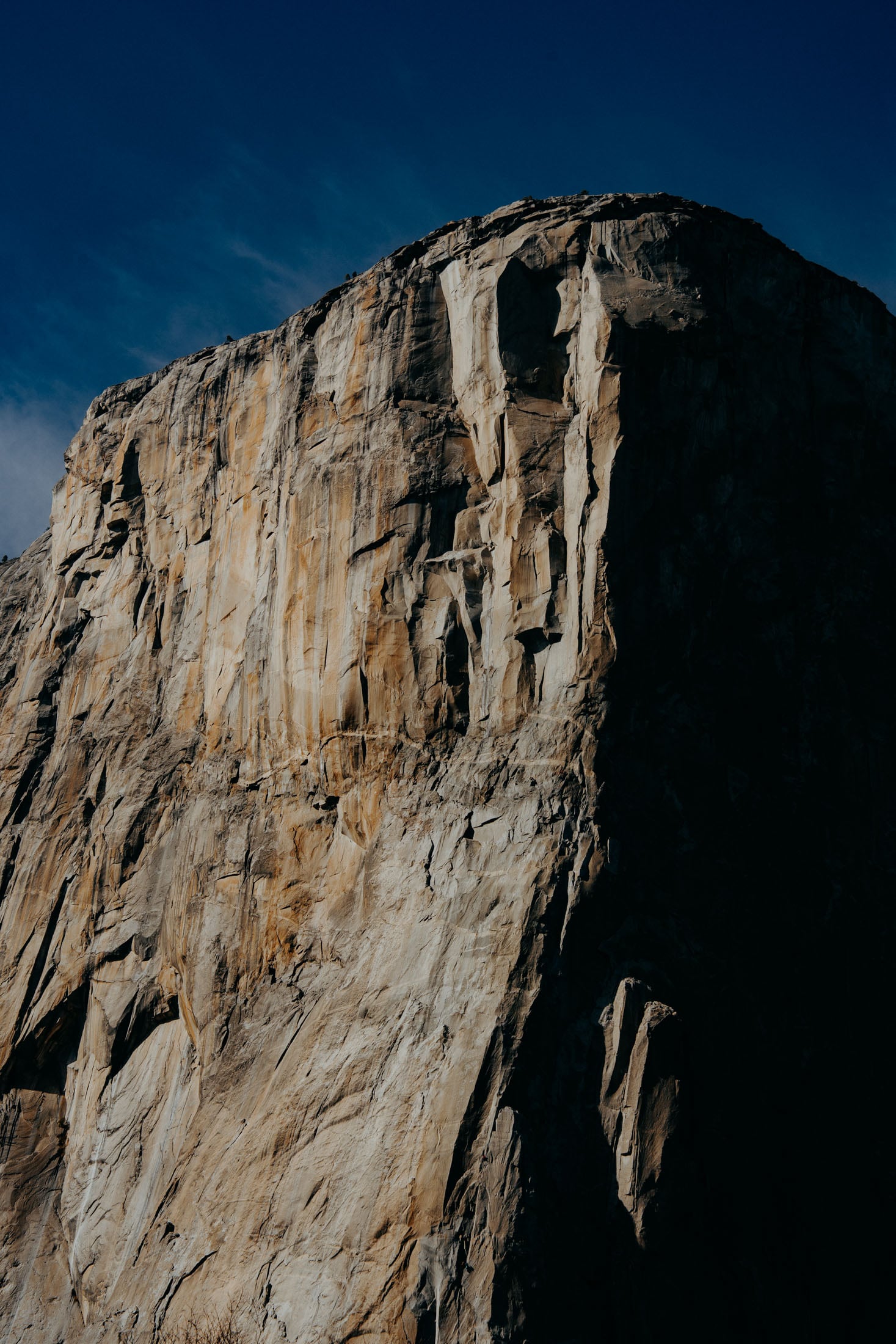 Close-up view of a towering rock face with intricate details and shadows under a clear blue sky.