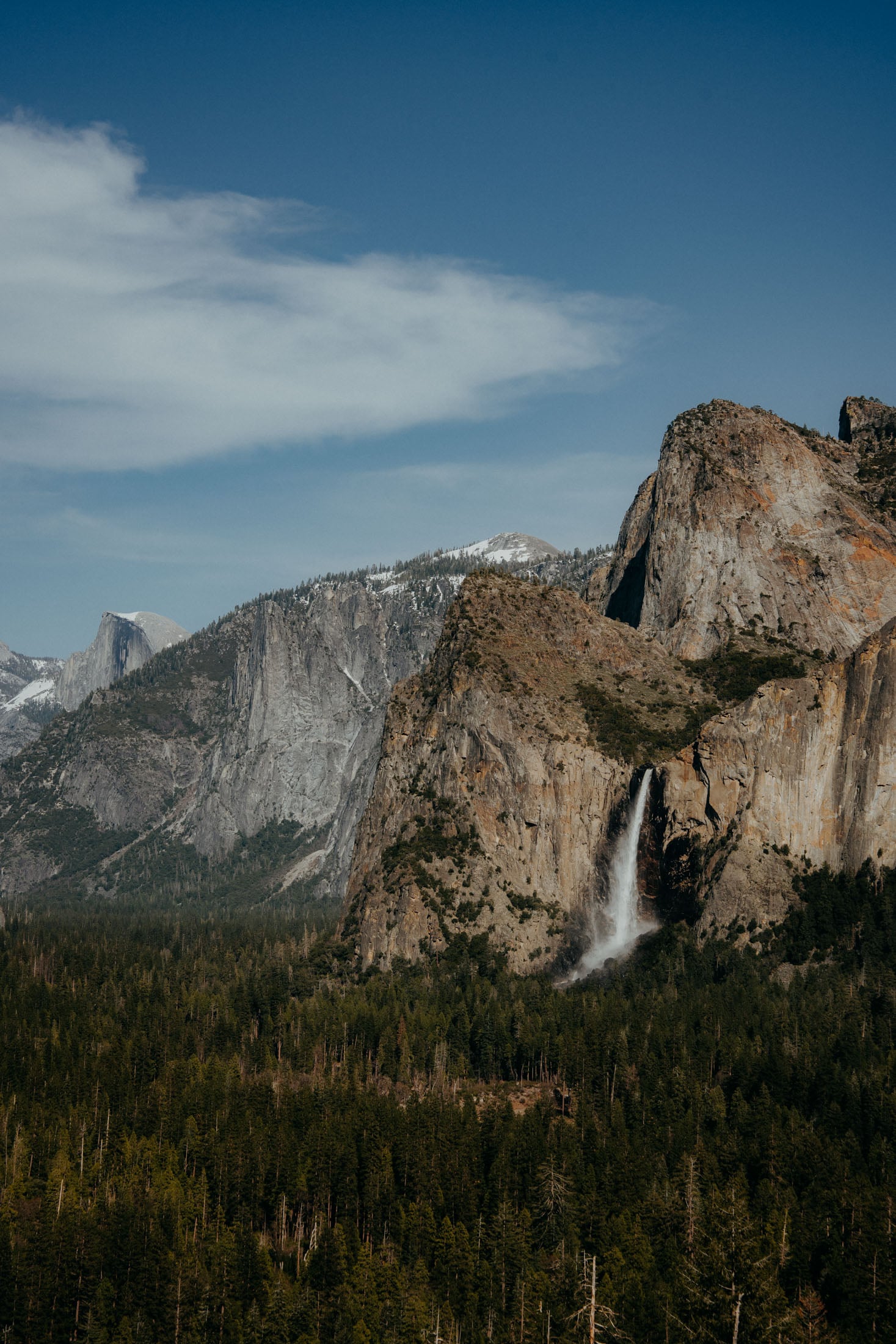A breathtaking view of Yosemite National Park featuring towering granite cliffs and a cascading waterfall surrounded by lush green forests under a clear blue sky.