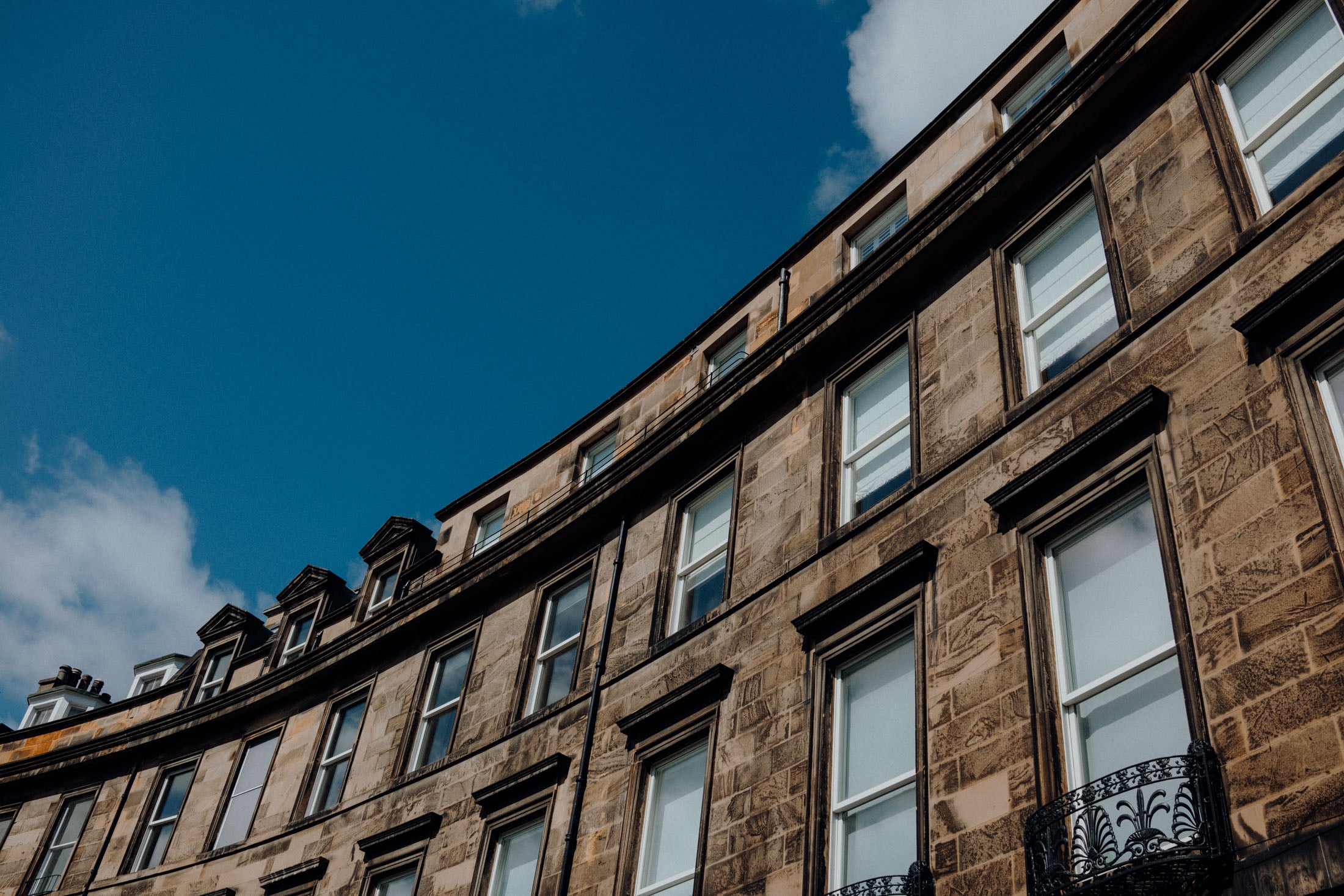 A curved building facade with multiple windows under a bright blue sky with a few clouds.