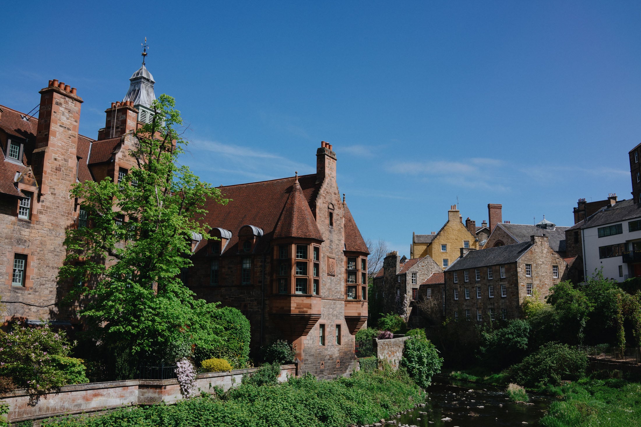 A scenic view of historic buildings along a river with lush greenery and a clear blue sky.