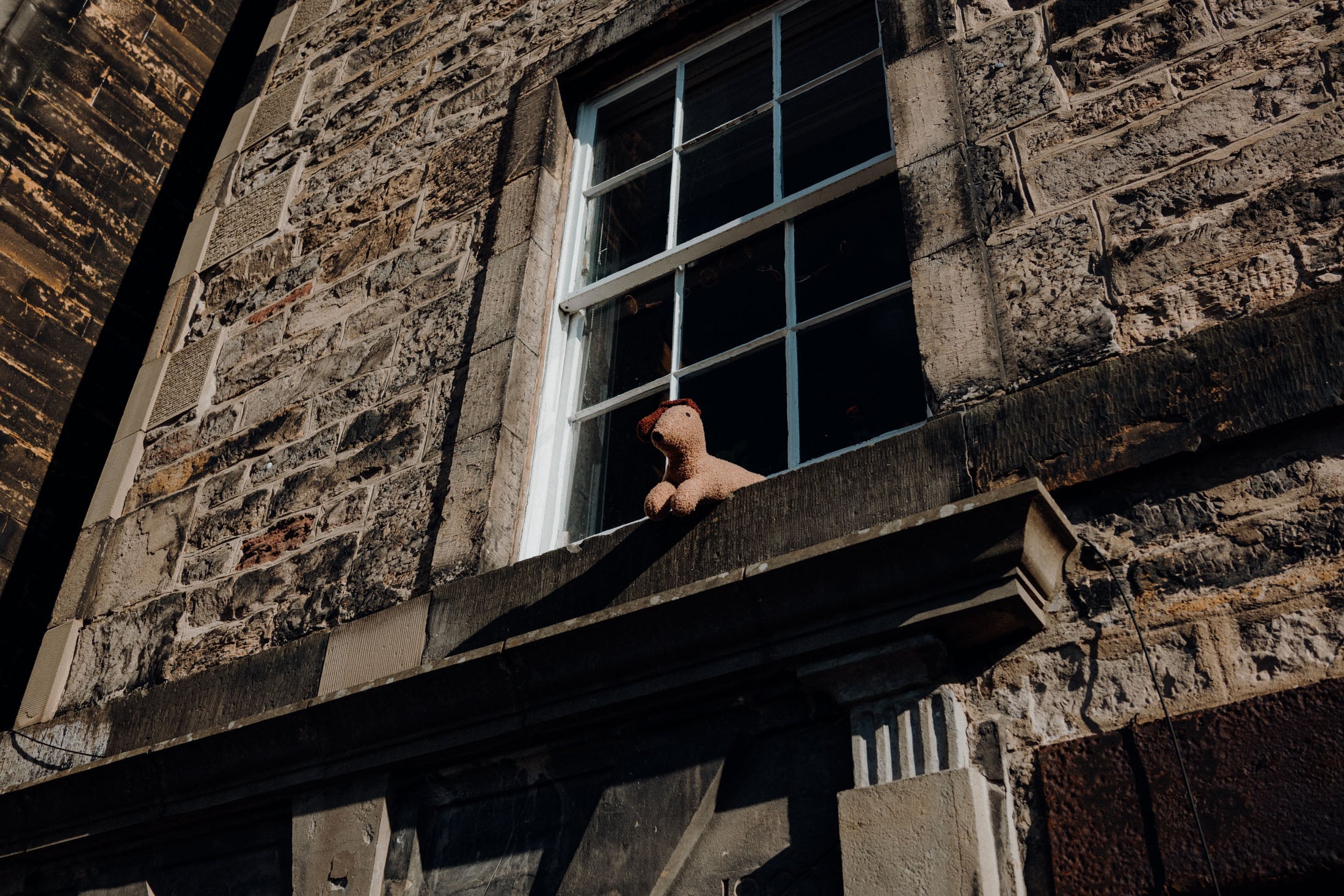 A stuffed toy dog sitting on a windowsill of a stone building.