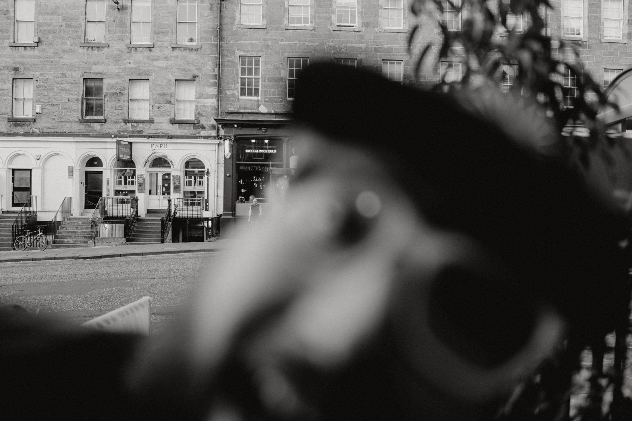 A blurred black and white image of a street scene featuring buildings with the name 'PAPI' on one of the storefronts, suggesting a lively urban area.