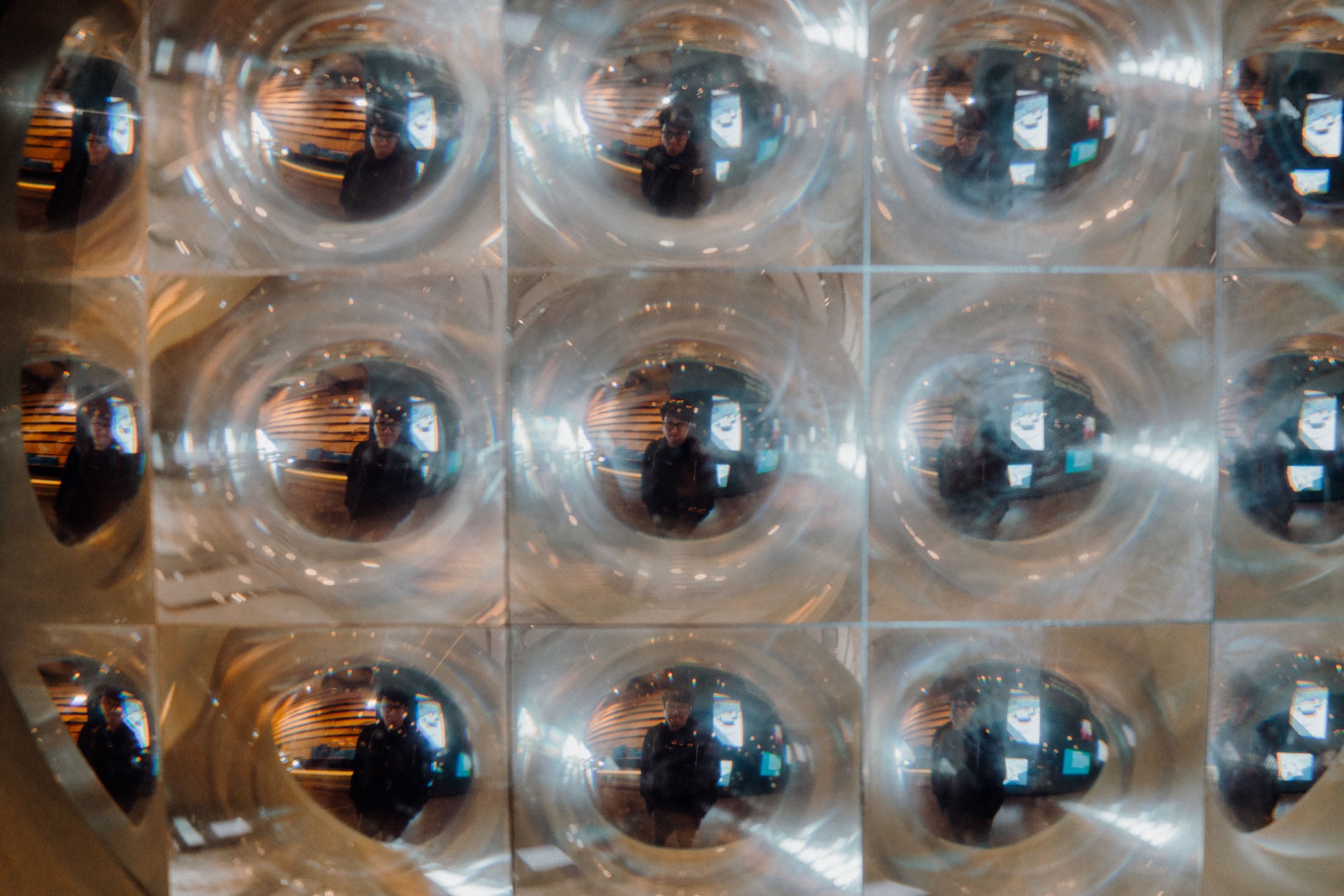 A grid of reflective glass bubbles capturing distorted reflections of a person and the surrounding environment.