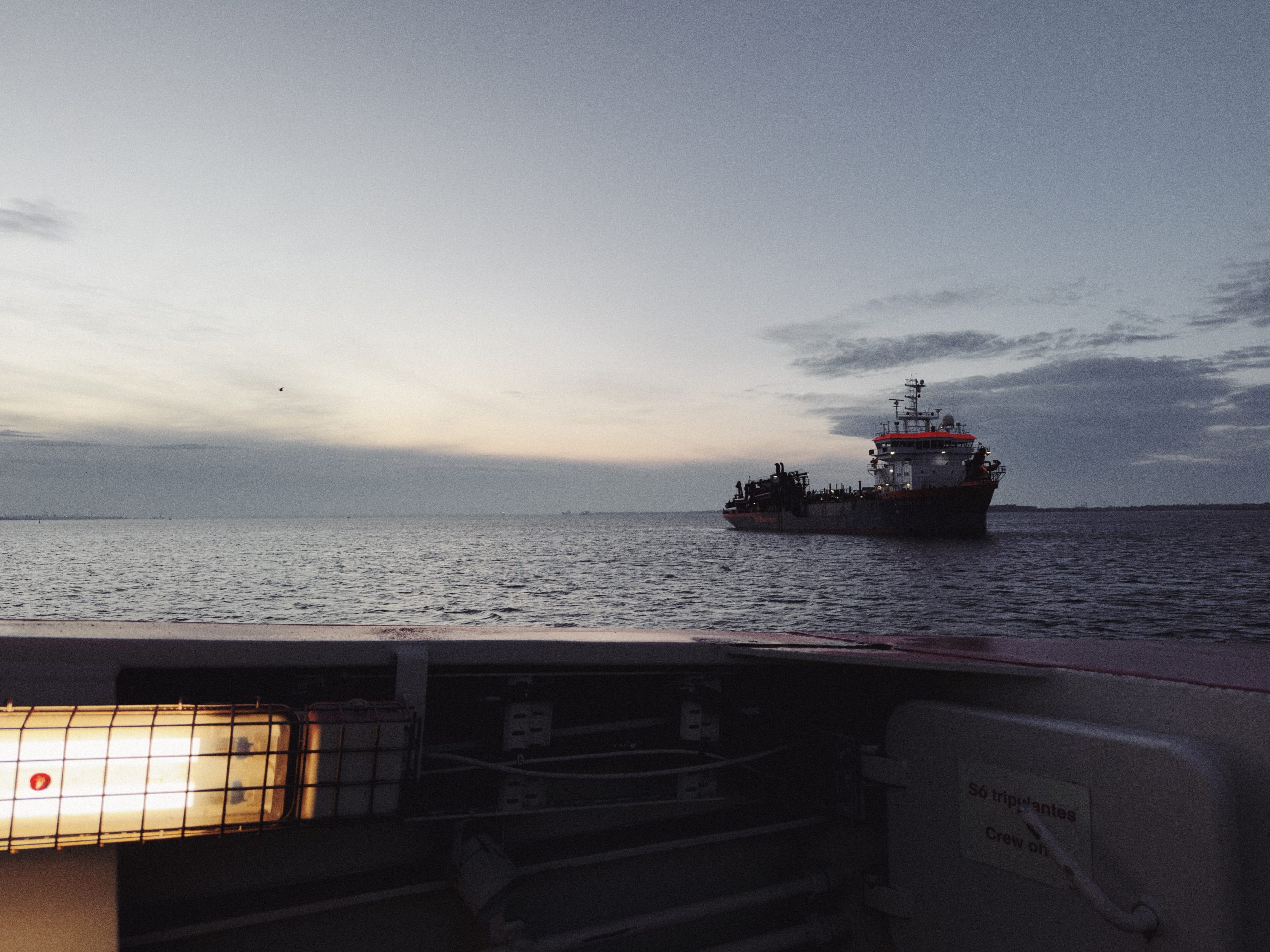 A view of a ship near the shore during dusk, with a calm sea and a gently lit sky.