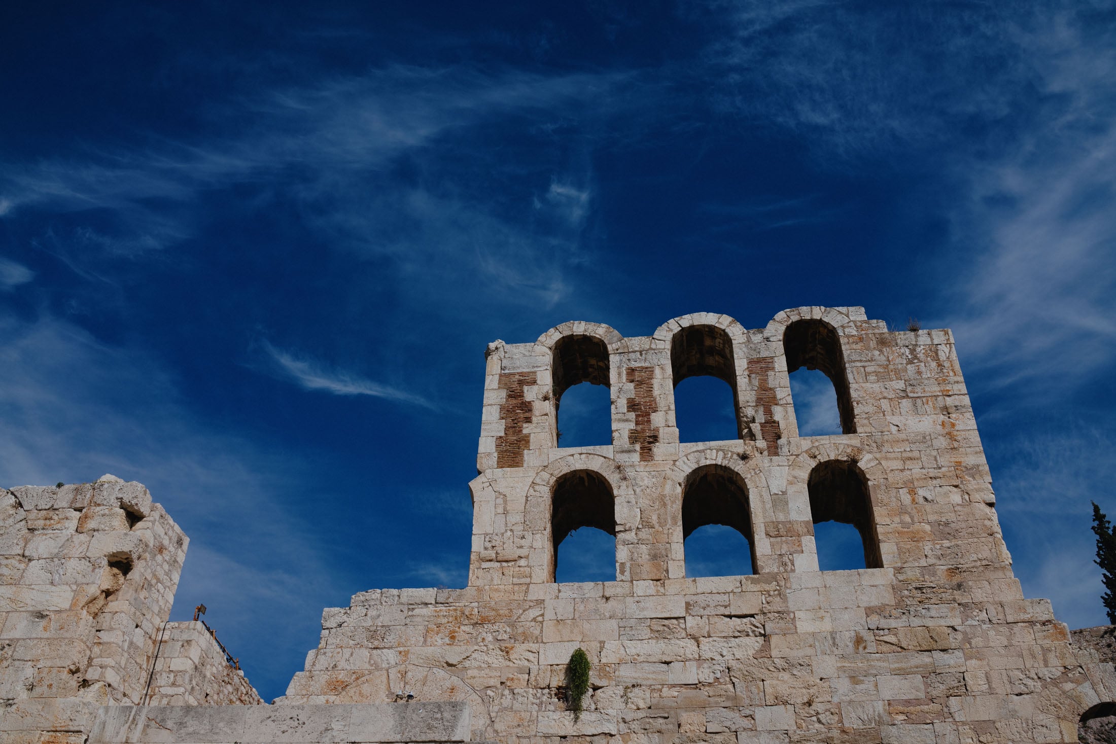 Remains of an ancient stone structure with arched openings against a blue sky.