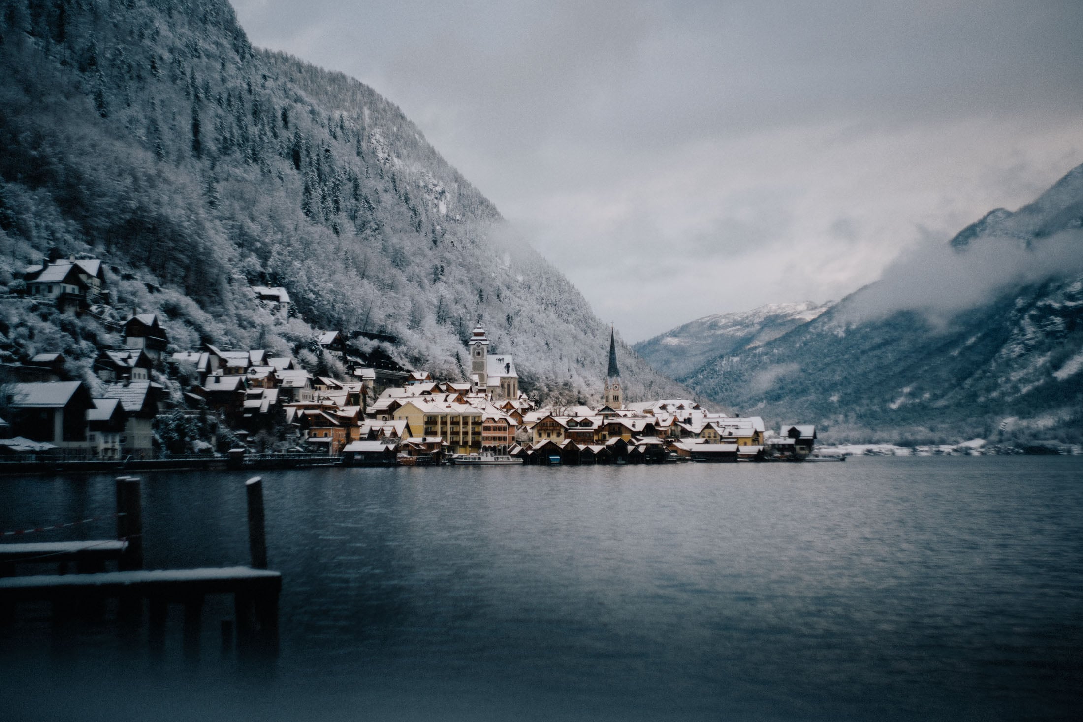 A picturesque winter scene featuring a quaint village surrounded by snow-covered mountains and a serene lake.
