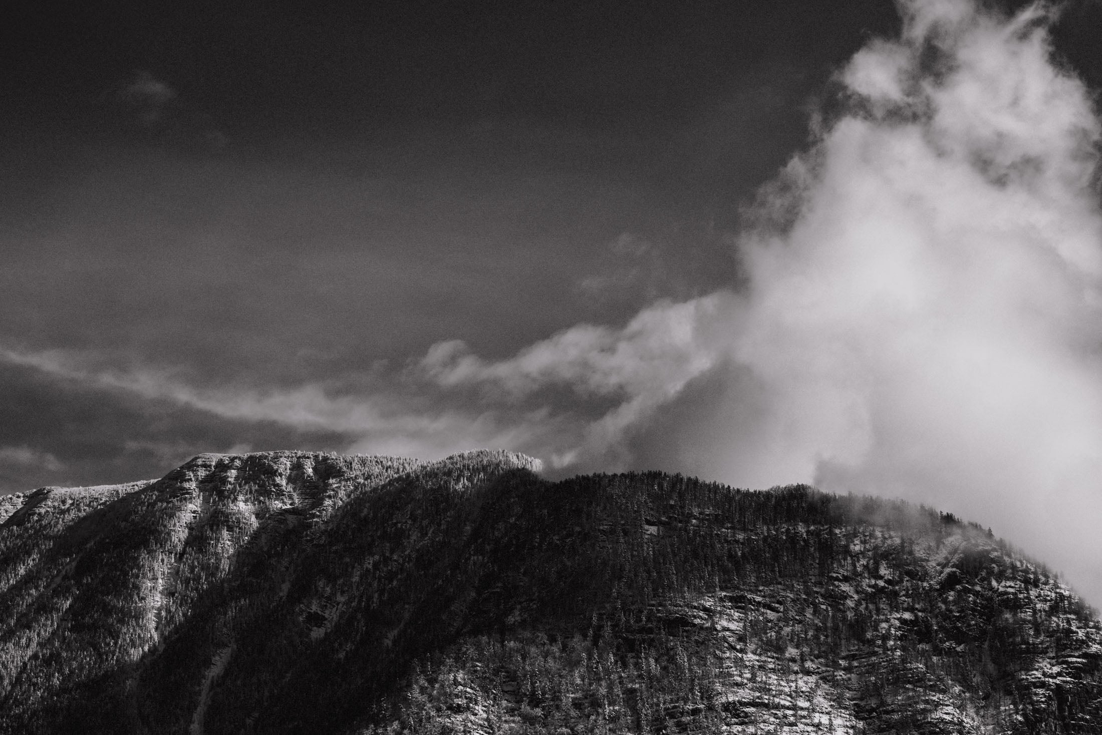 Black and white image of a rugged mountain range under a cloudy sky.