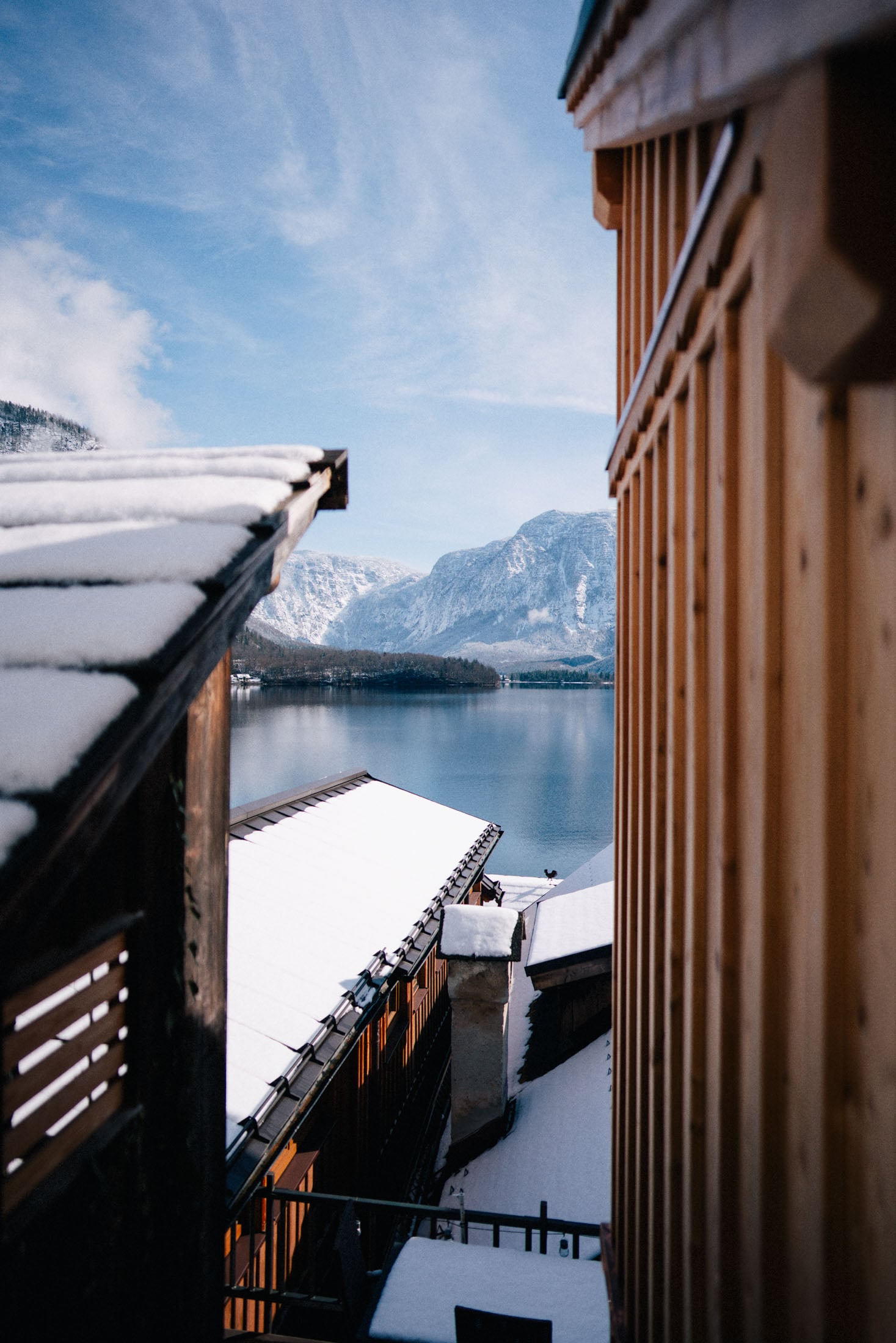 Snow-covered rooftops overlooking a calm lake and mountains under a clear blue sky.