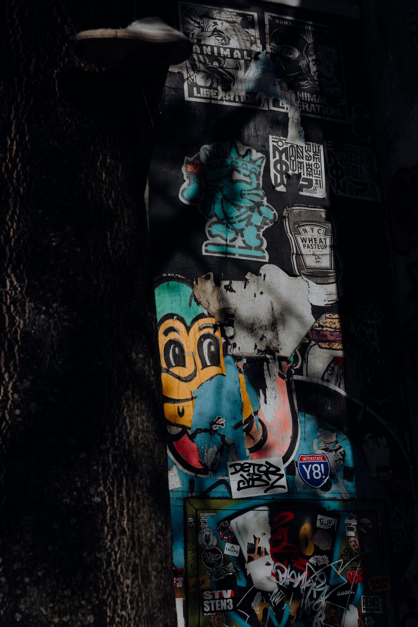 A wall covered in colorful street art and graffiti, featuring various stickers, images, and tags, illuminated by subtle shadows.
