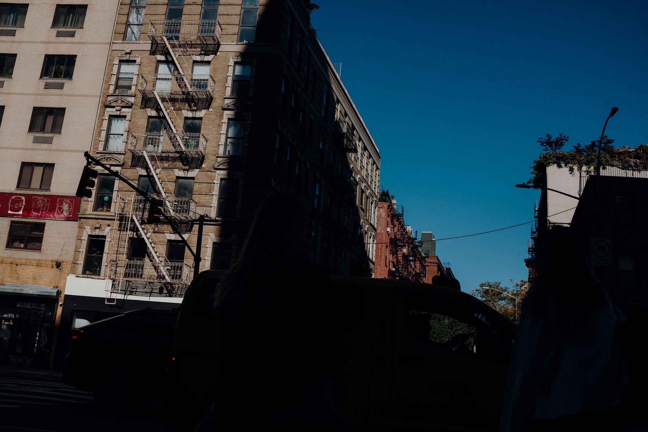 Silhouetted figures in front of urban buildings with fire escapes, under a clear blue sky.